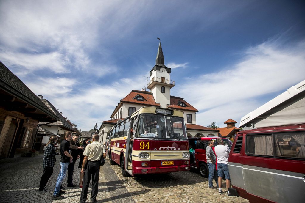 Na płycie rynku Miasteczka Galicyjskiego stoi stary zabytkowy autobus. Fotograf zrobił zdjęcie przez boczną szybę, ze środka autobusu. Widać przez nią osoby, które oglądają inne pojazdy.