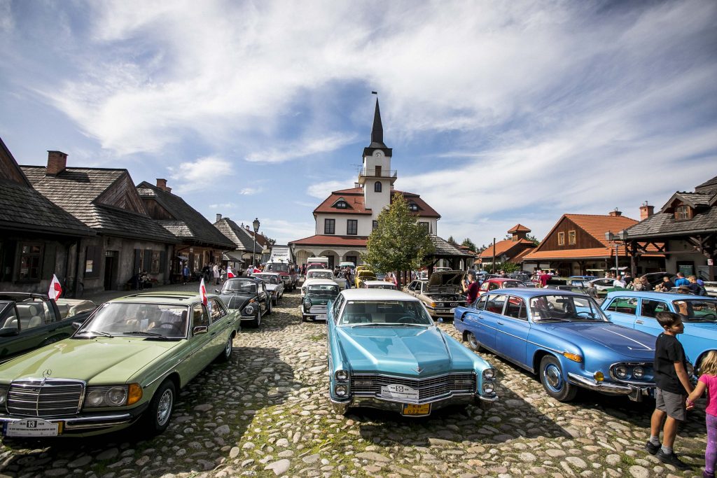 Na rynku Miasteczka Galicyjskiego odbywa się XII Zlot Zabytkowych Pojazdów. Na pierwszym planie znajduje się zabytkowy samochód, który ma lakier w błyszczącym niebieskim kolorze. 