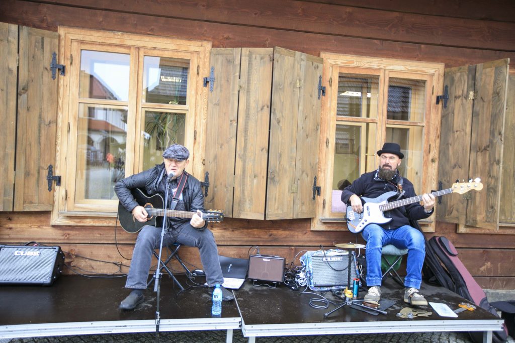 Dwóch muzyków gra na tle budynku kasy Miasteczka Galicyjskiego podczas Kiermaszu Staroci. Jeden z nich śpiewa i gra na gitarze akustycznej, drugi gra na gitarze basowej.