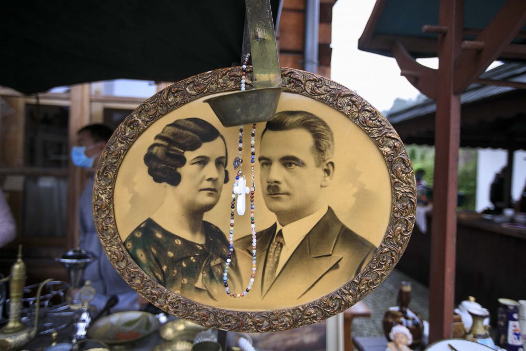 - Na straganie jest zawieszona stara fotografia w okrągłej ramce, która przedstawia kobietę i mężczyznę w strojach z lat dwudziestych dwudziestego wieku. 