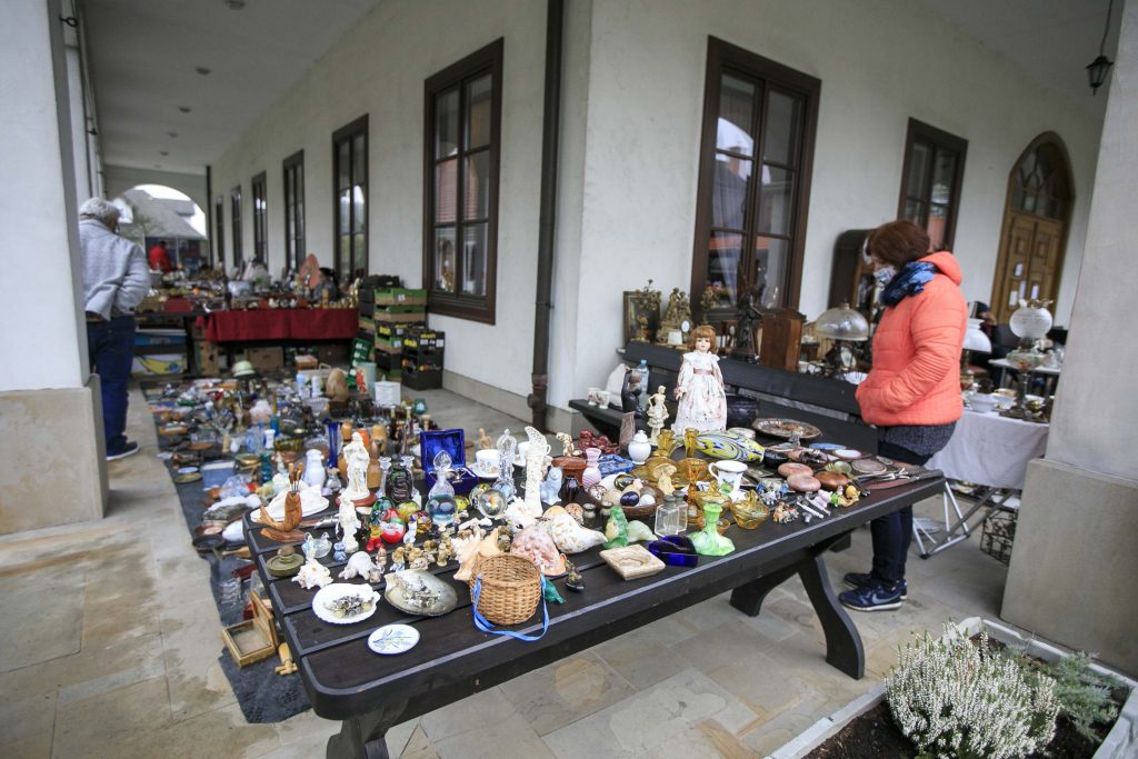 Stoisko z bibelotami stoi na rynku w Miasteczku Galicyjskim podczas Kiermaszu Staroci. Na stoisku znajdują między innymi porcelanowe figurki, cukiernice, świeczniki z żółtego szkła, srebrne łyżki do sałaty.