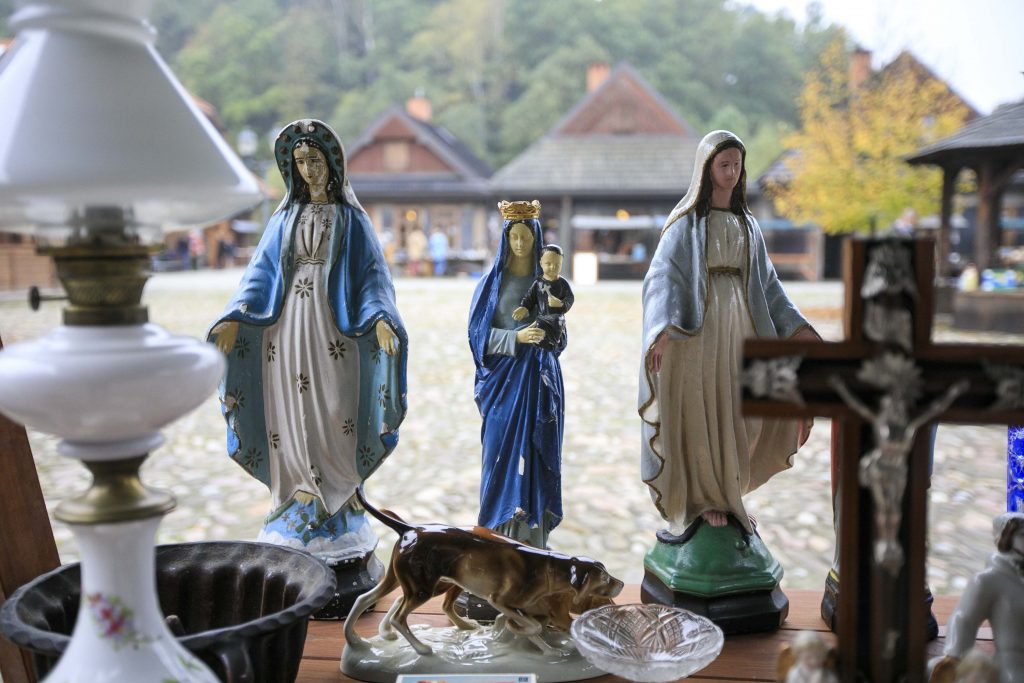 Na stoisku stoją figurki Matki Boskiej i Matki Boskiej z Dzieciątkiem oraz krzyż wykonany z drewna z ukrzyżowanym Jezusem. Figurki są niewielkie i kolorowe. 