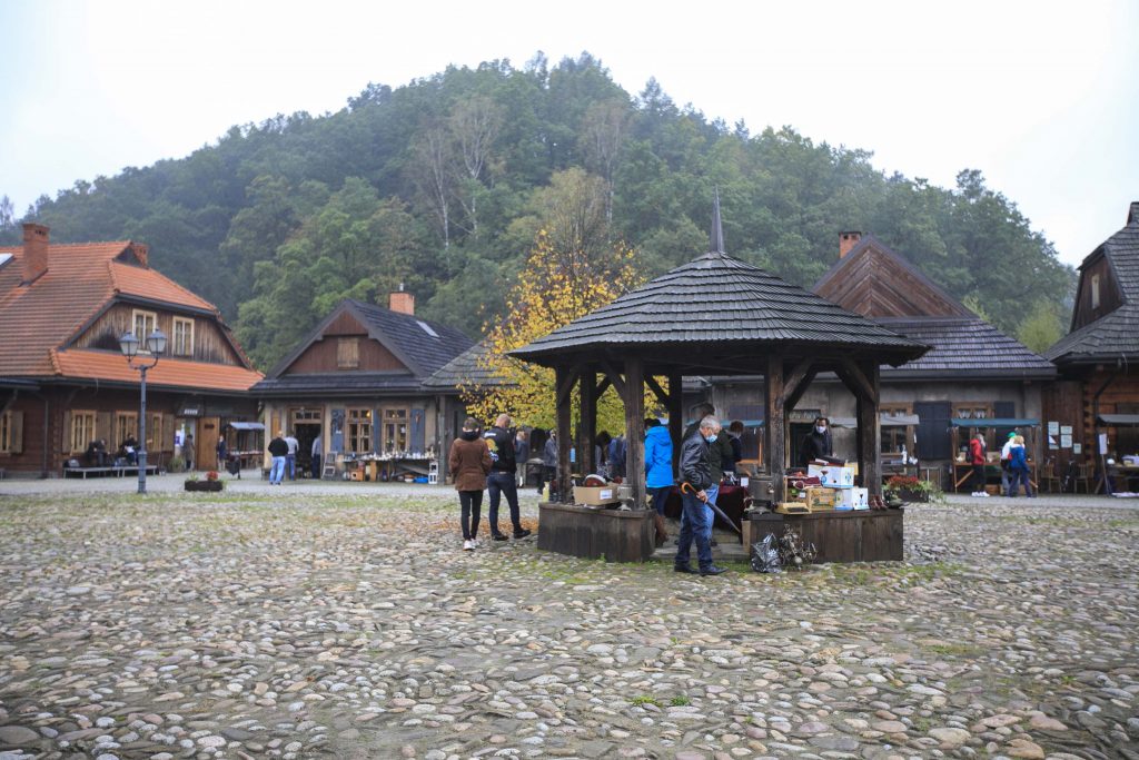 Na środku studni Miasteczka Galicyjskiego znajduje się stoisko z bibelotami. Obok niego przechadzają się ludzie i oglądają rzeczy. 